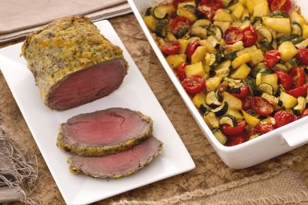 Roast beef with citrus fruits with a tray of potatoes, zucchini, and cherry tomatoes